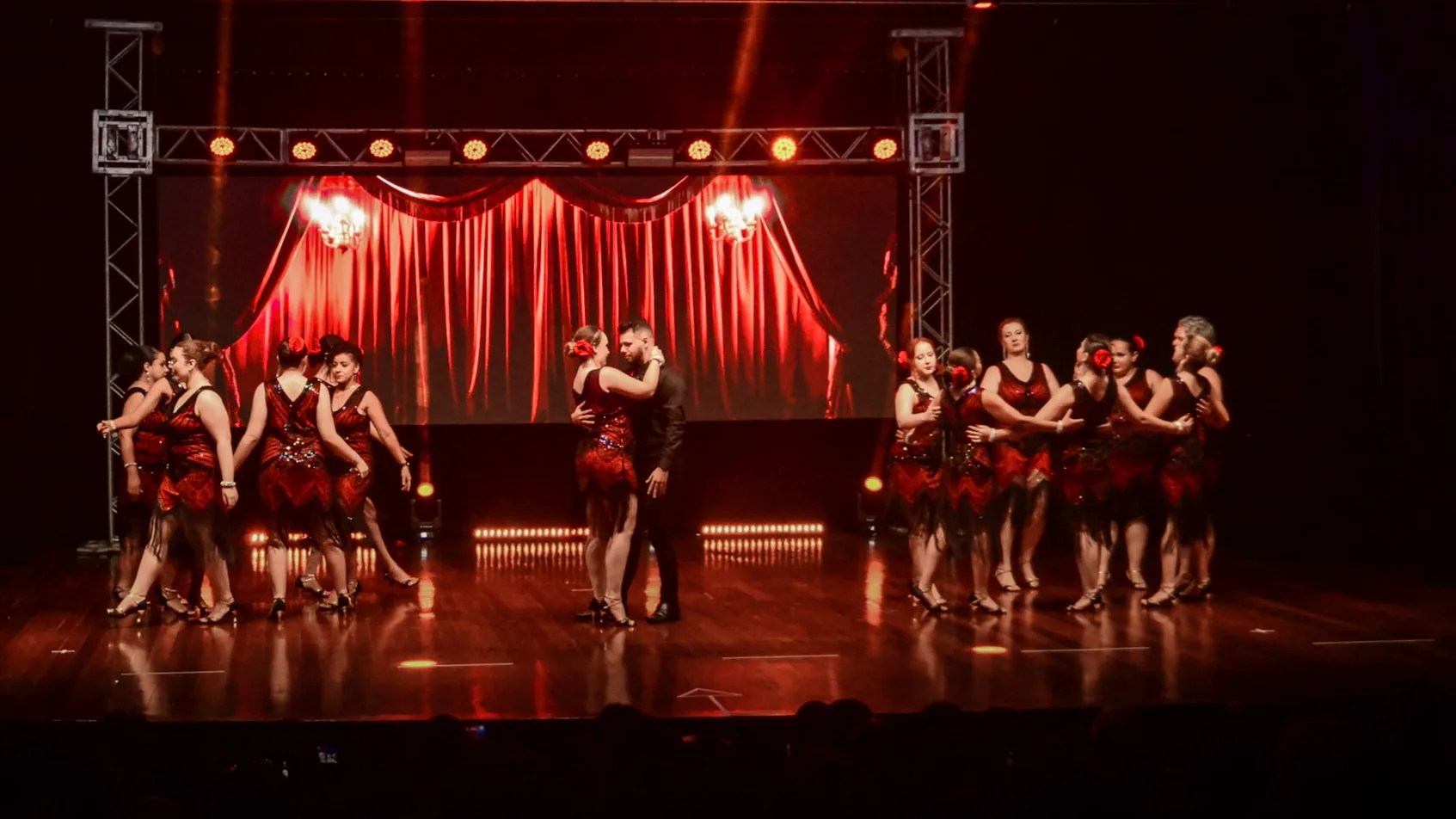 Apresentação coletiva de dança em palco com cortina e luzes vermelhas.