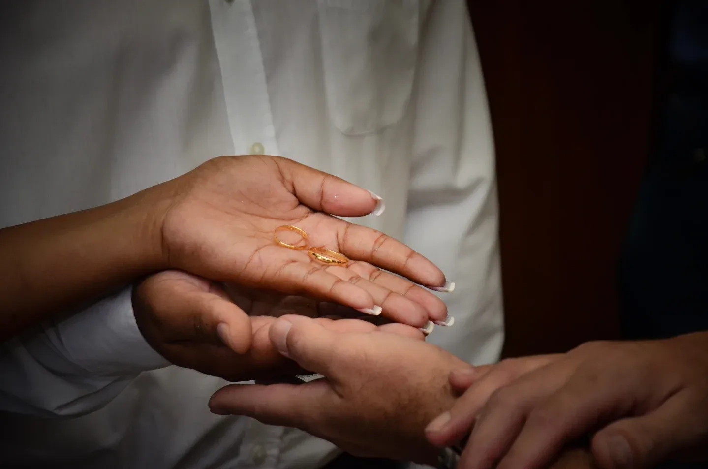 Detalhe das mãos e alianças durante casamento.