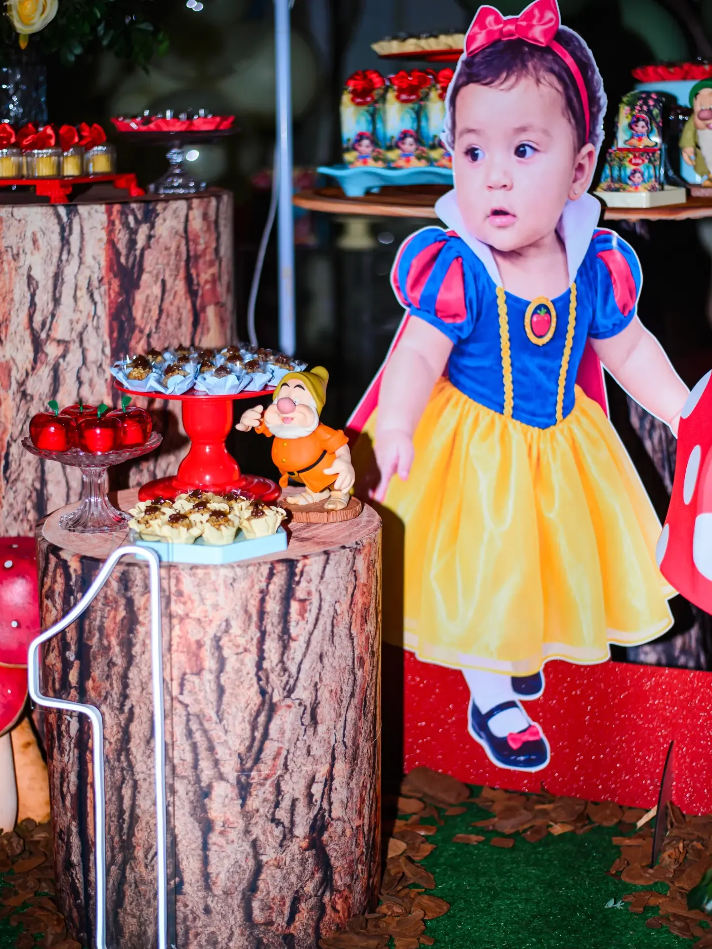 Criança com vestido colorido ao lado de mesa de aniversário.