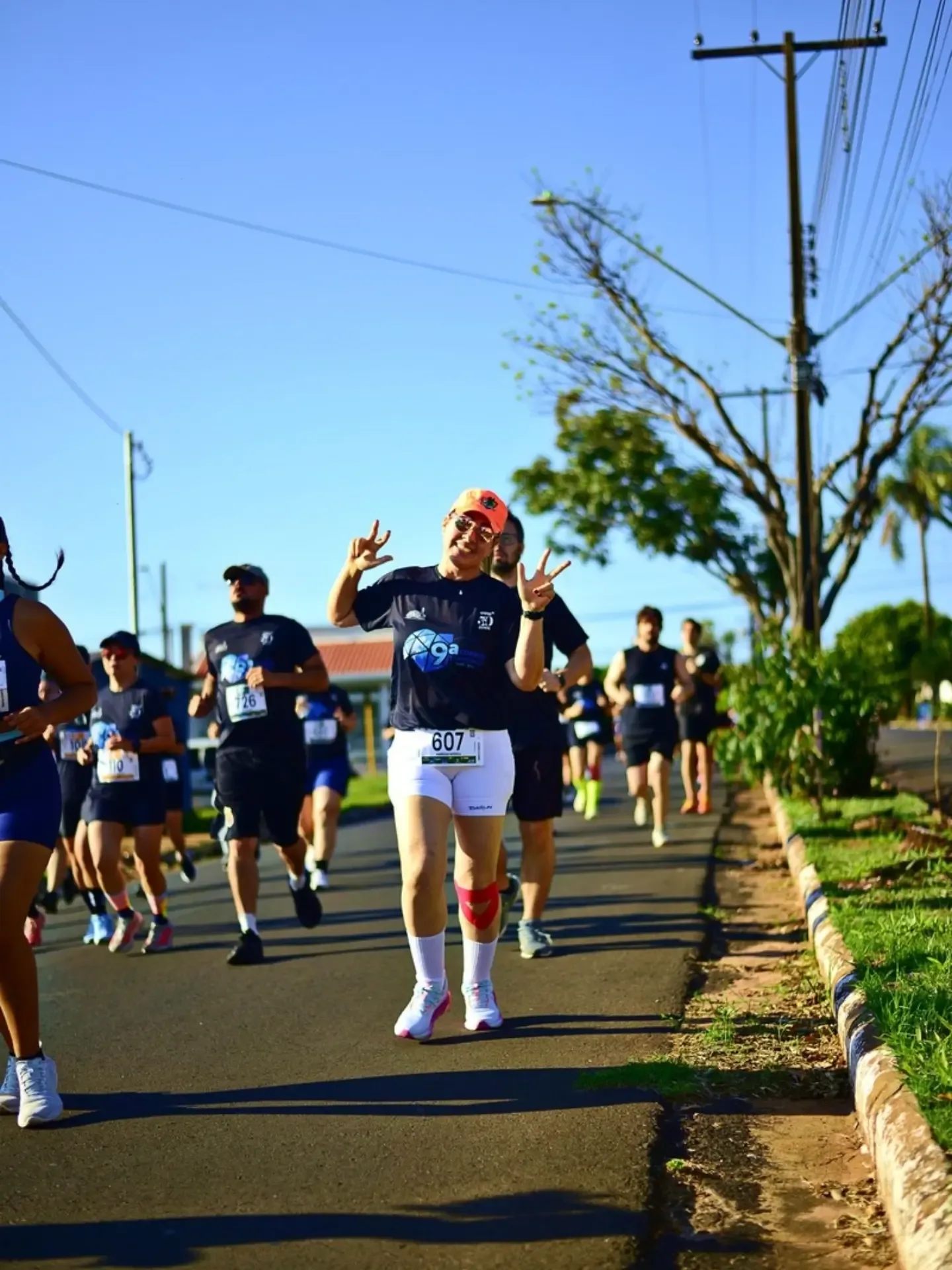 Participantes de corrida em rua com árvores e casas.