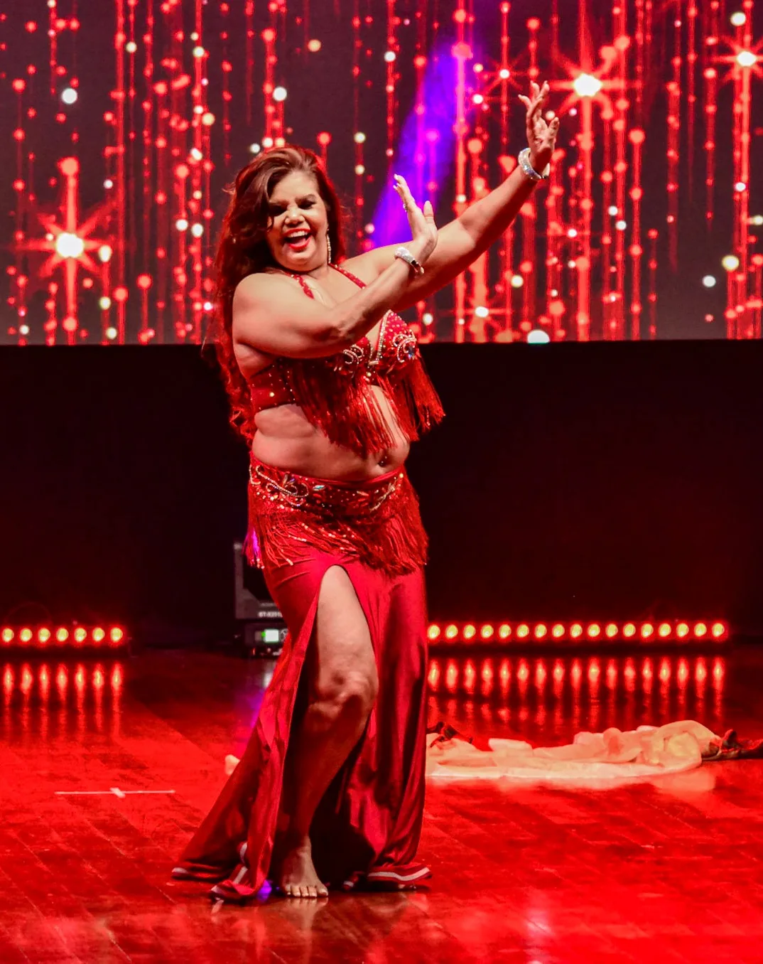 Dançarina com figurino vermelho e um braço erguido no palco.