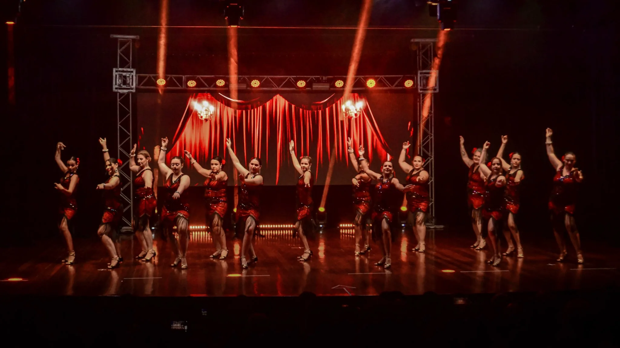 Grupo de dança em palco amplo com iluminação vermelha.
