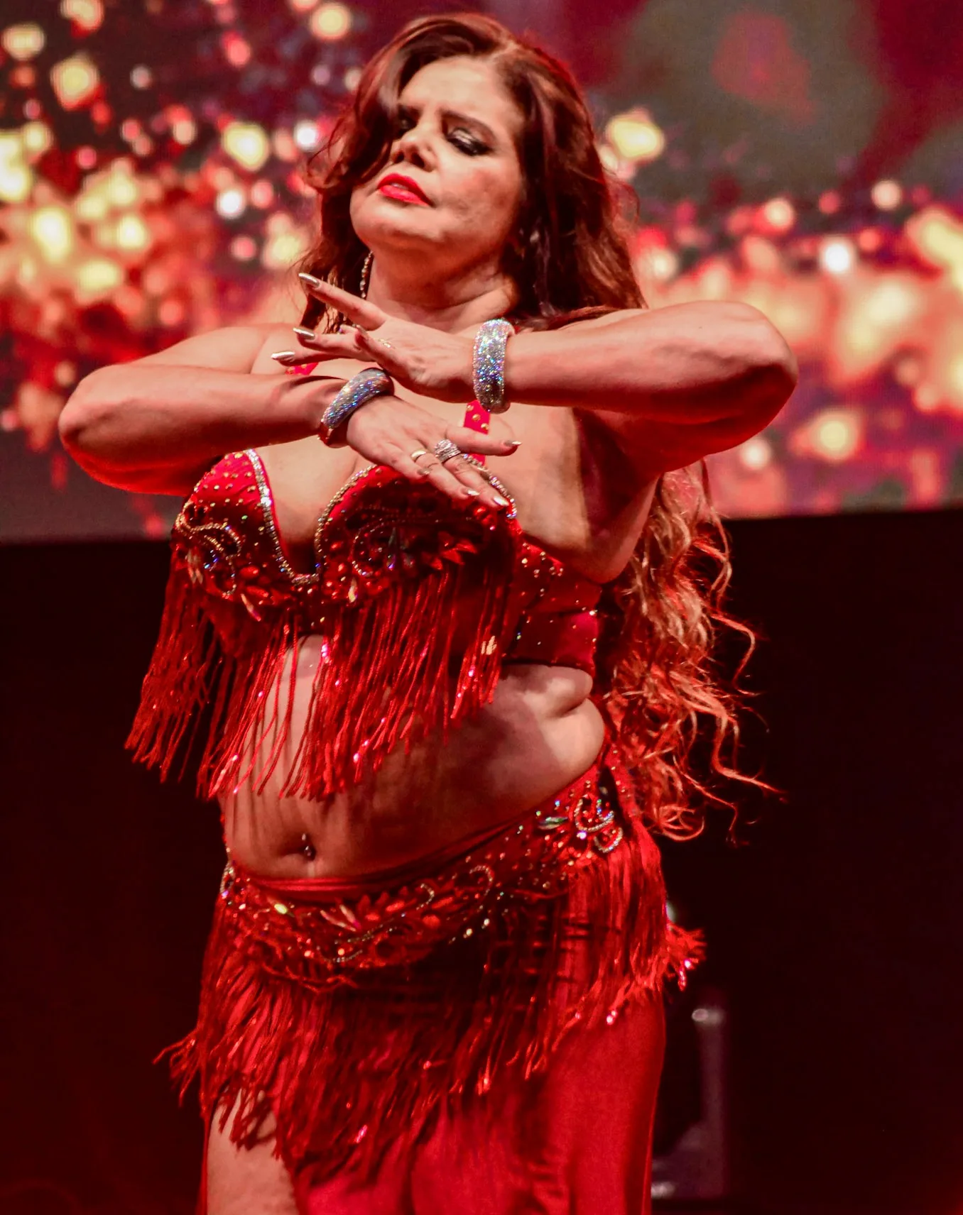 Dançarina com figurino vermelho e as mãos próximas ao rosto.