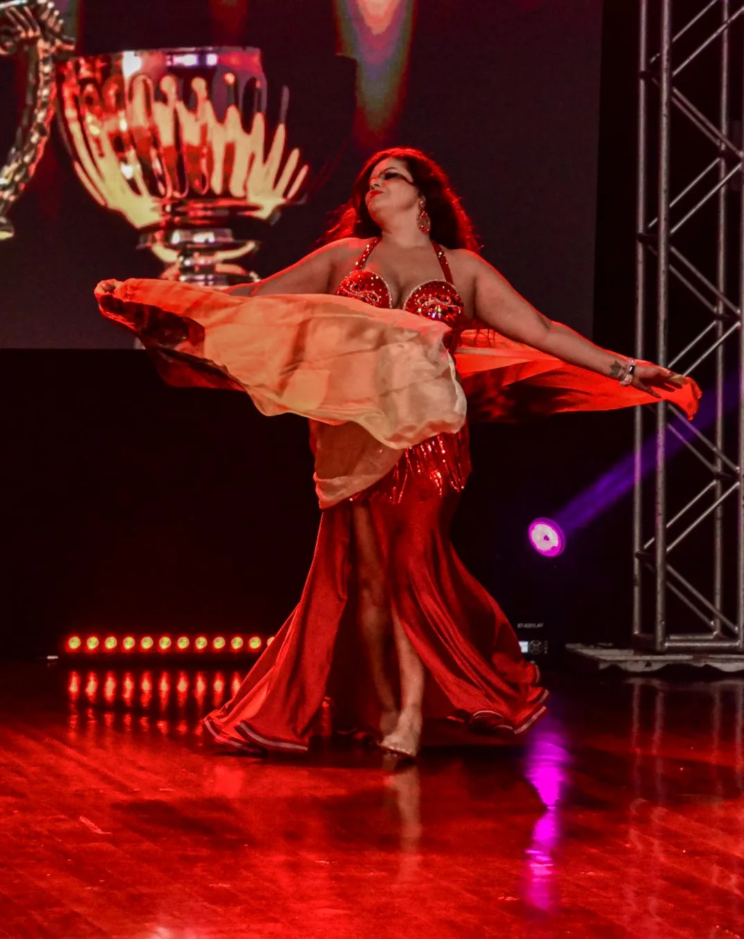 Dançarina com figurino vermelho movimentando os braços no palco.
