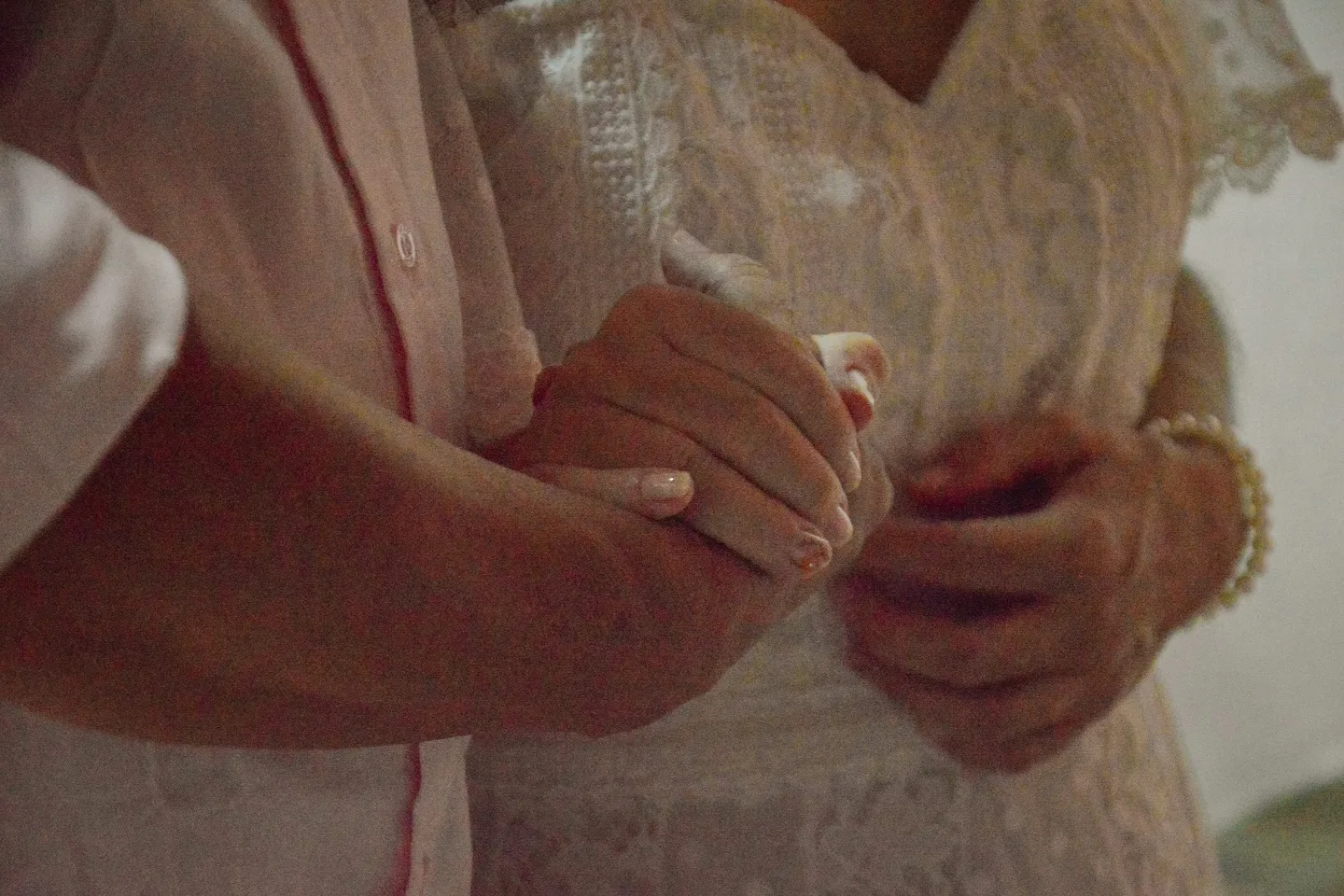 Detalhe das mãos e das roupas do casal durante casamento.