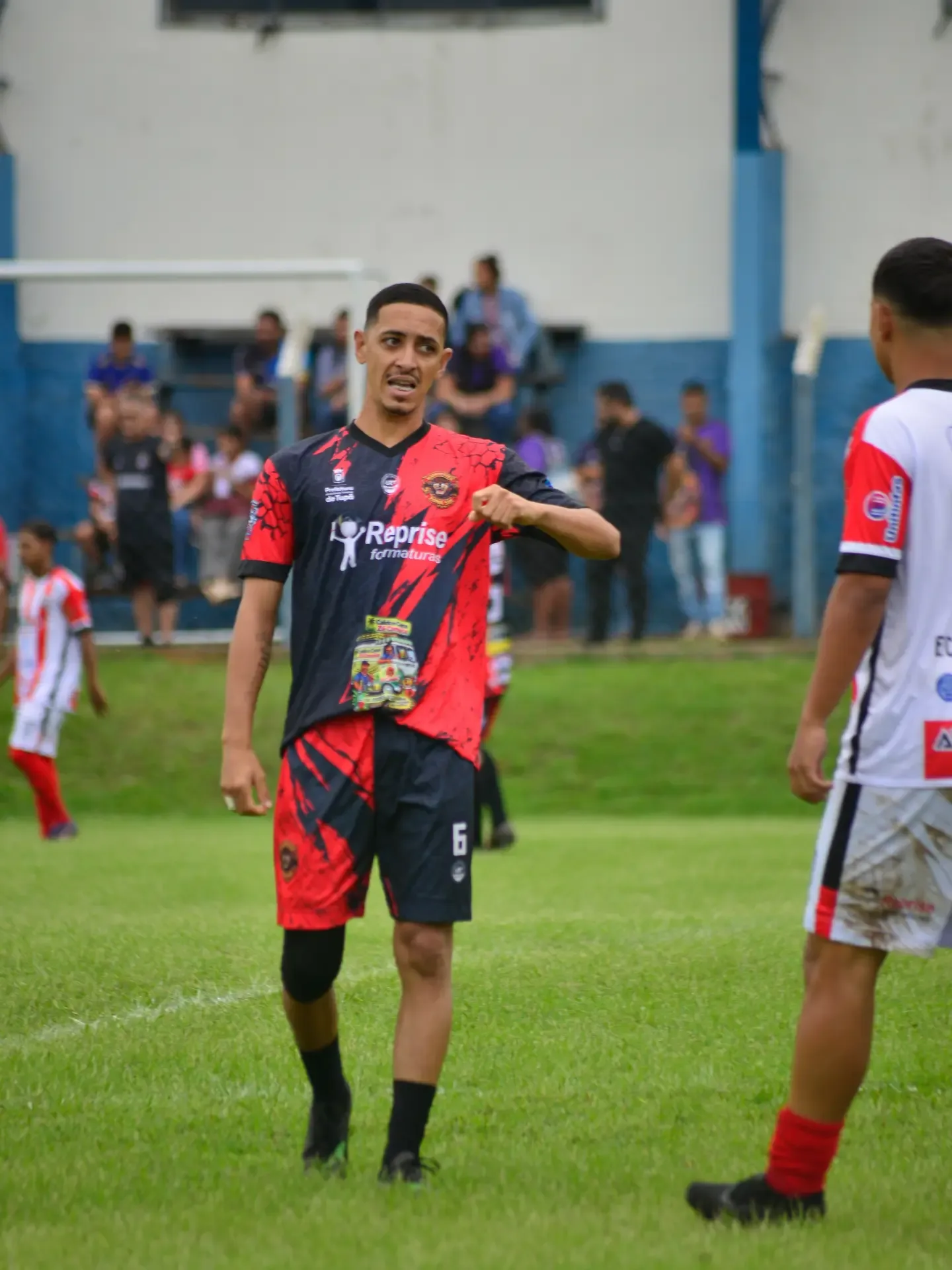 Jogador de futebol com uniforme vermelho e preto gesticulando no campo.