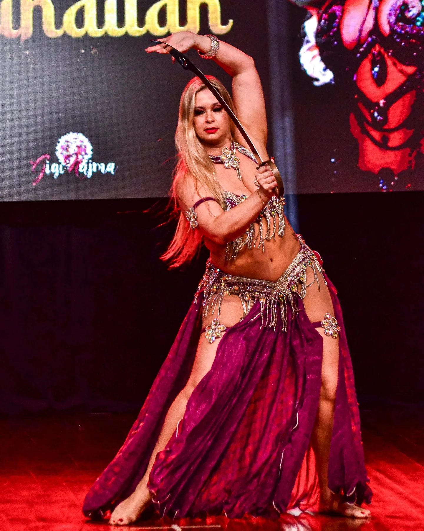 Dançarina com um braço erguido em palco com iluminação vermelha.