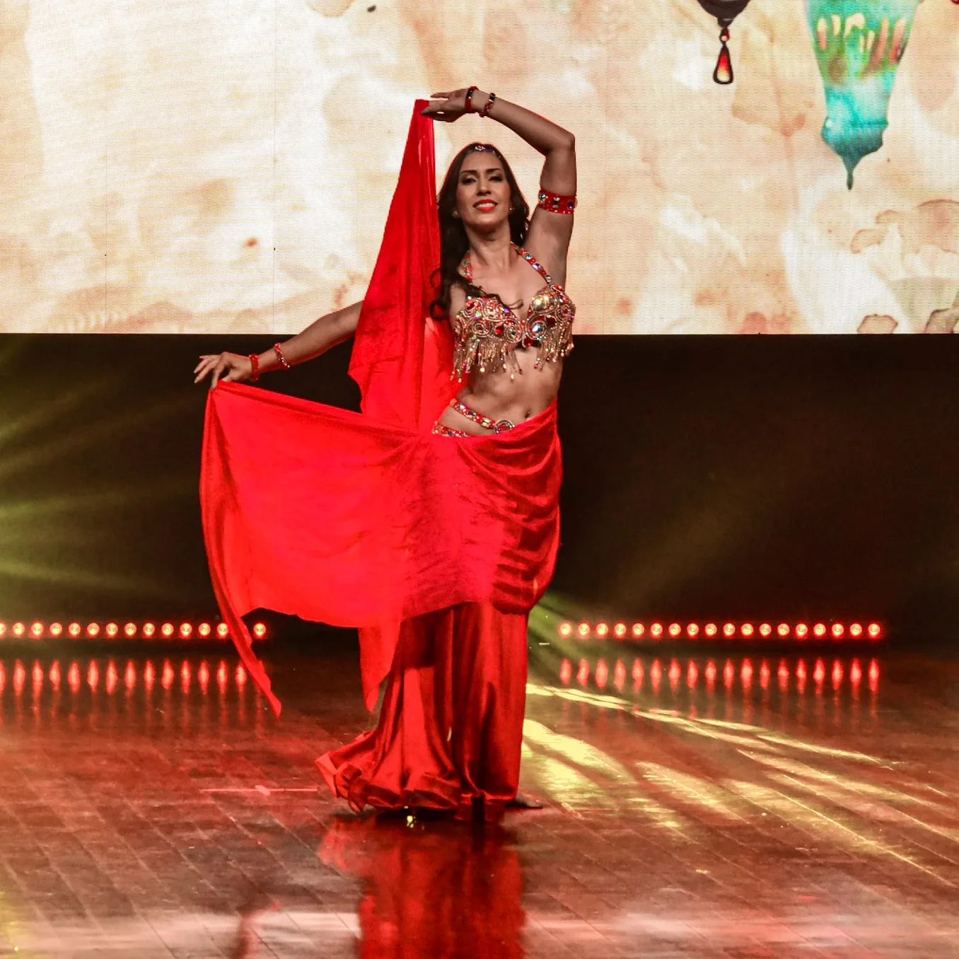 Dançarina com véu vermelho e um braço erguido no palco.