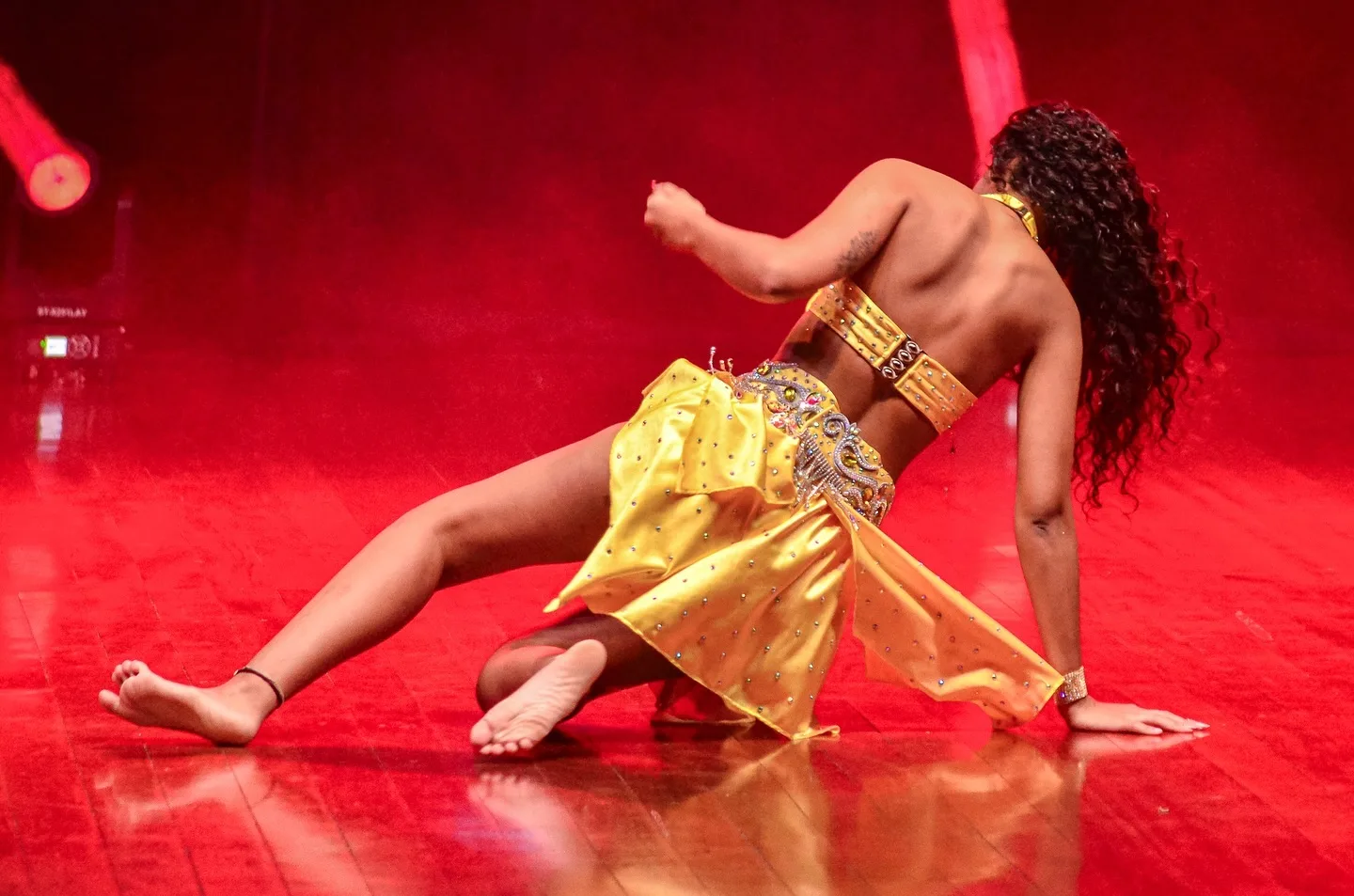 Dançarina em movimento no chão de um palco iluminado de vermelho.