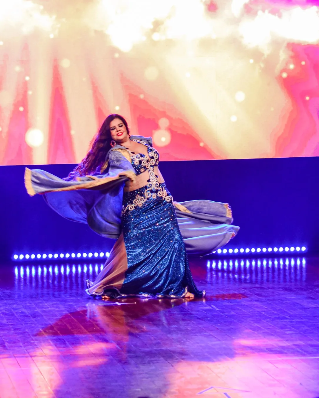 Dançarina girando com figurino azul e tecido em movimento.