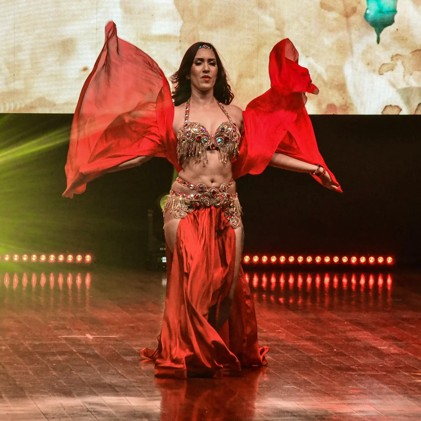 Dançarina com véu vermelho aberto dos dois lados durante apresentação.