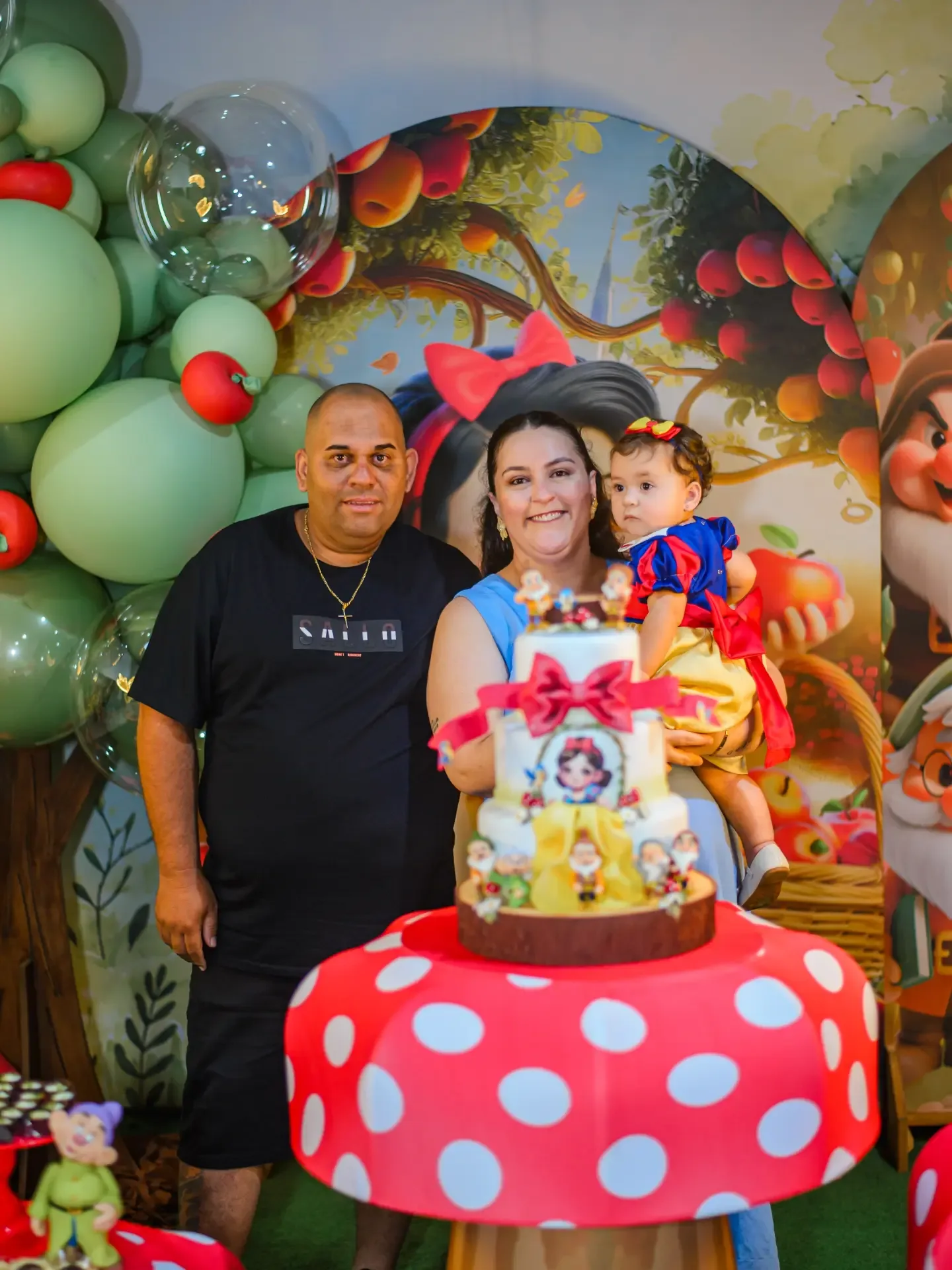 Três pessoas reunidas diante da mesa de uma festa de aniversário.